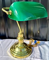 Front and side view showing gilded brass tiered base, brass arm, and curved green glass shade with pull chain