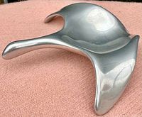 Pewter goose sculpture resting on a pink fabric with a smooth shiny surface and signature visible on the bottom side.