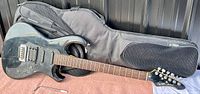 Full view of the black electric guitar with a soft gig bag in background, showing the body and neck with some surface scratches.