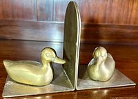 Side view of the brass duck bookends showing one duck in a sitting pose on an L-shaped base.