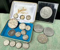 Overall view showing multiple vintage silver coins and medallions on a surface and displayed in a blue-lined Jewelry Originals case and a black display box.