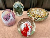 Photo showing all four glass paperweights arranged in a group on a flat surface, highlighting their shapes and colors.