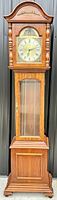 Front view of full grandfather clock showing wooden case and glass door at base.