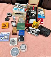 Overview of the full lot including the vintage Ricoh 35mm film camera, leather camera case, user manual, multiple filters, flash unit, lens adapters and other camera accessories lying on a pink fabric background.