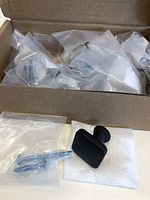 Box opened showing multiple individually bagged black square drawer knobs with screws inside the box and one knob and screw outside the box on a white surface.