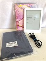 Amazon Kindle and accessories arranged on white surface, showing the Kindle in front of two cases and the charging cable