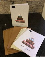 Photo showing multiple plantable Happy Birthday cards with printed cake image and 'PLANT ME!' sticker, alongside matching brown envelopes.