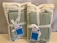 Photo showing two sets of kitchen linens packaged with white ribbon and tags, each set containing a striped towel and two dishcloths.