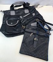 Two purses on white background: large black nylon tote bag with external flap pocket and handles, smaller black crossbody purse with decorative cut-out pattern