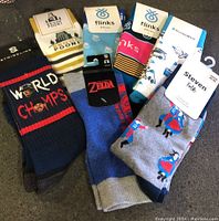 Seven pairs of men's socks arranged for display, showing multiple brands and designs, including text, character, travel themes, and folk dancers.
