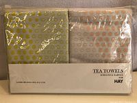 Packaged set of two tea towels in olive green and beige with gold Landscape Dots patterns.