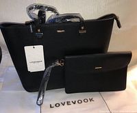 Set of two black bags from Lovevook, large purse with handles and smaller clutch with wrist strap on branded cloth mat, showing tags and packaging.