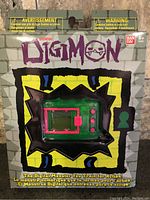 Front view of sealed Digimon Tamagotchi virtual pet packaging with device visible in blister pack showing green and pink digital pet.