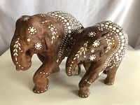 Pair of wooden elephant statues with white floral and dot painted patterns, showing missing tusks with small holes.