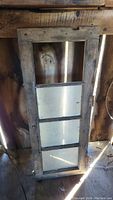 Barn window leaning against a wooden wall showing entire frame and three glass panes