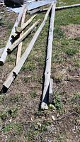 Several cedar wood beams of various lengths and thicknesses laid on grassy ground, some with bark and rough surfaces visible.