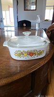 Front and side view of CorningWare casserole dish showing the La Marjolaine vegetable and fruit design on white ceramic with glass lid.