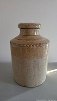Front view of vintage stoneware crock showing cylindrical shape, beaded detail near top, and beige to brown glaze.