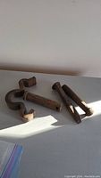 A group photo showing four iron items including a railroad spike, curved iron hook, iron bolt, and threaded iron rod with visible rust and wear.
