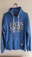 Front view of blue Jack and Jones hoodie with logo print and white drawstrings on hanger.