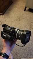 Photo showing the right side and front of the black JVC GR-HD1 camcorder with lens cover on, held in hand.