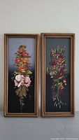 Two framed original floral paintings side by side, with vertical black or dark backgrounds and colorful flowers