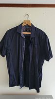 Men's short sleeve navy blue shirt with small dots, hanging on a wooden hanger.