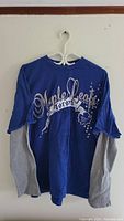 Blue Toronto Maple Leafs long sleeve T-shirt with layered grey sleeves hung on white hanger against wall