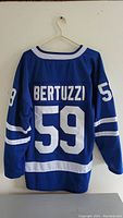Back side of the blue Toronto Maple Leafs hockey jersey showing white number 59 and Bertuzzi name, white stripes on sleeves and bottom hem, hanging on plastic hanger.