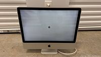 Front view of Apple iMac computer with Apple logo on screen, powered on but untested.
