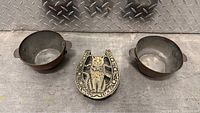 Photo of two large brass bowls and one decorative brass horseshoe with owl and 'Good Luck' engraving on metal diamond plate floor.