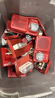 Large bin filled with multiple red vintage fire alarm horns with clear strobe lights and wiring inside.