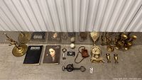 Overview of the lot showing brass candlestick, clock, books, small camera, baseballs, and collectibles arranged on floor.