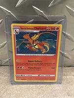 Photo showing Special Delivery Charizard Pokémon card protected in a rigid plastic sleeve standing on a beige surface.