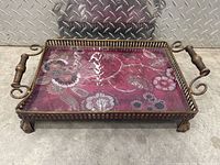 Front view of rectangular decorative tray with floral insert, metal border, wooden handles and feet.