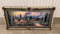 Full view of framed oil painting showing teepees, horses, forest and mountain landscape