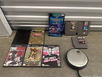 Full view of lot arranged on concrete floor showing PS2 cases, GameCube case, NES cartridges, boxed PC/Mac software and disc binder