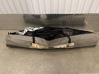 Closed gray carrying bag of the Woods Easy Up Screen House tent unrolled flat on the floor.