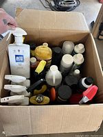Open cardboard box filled with assorted used auto cleaning bottles and spray containers in various sizes and colors.