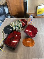 Photo showing various red and amber car tail and signal light lenses, some with attached wiring harness, arranged on a table.