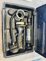 Open black plastic carrying case showing the cooling system pressure tester components including hoses, adapters, and pressure gauge.