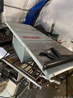 Angle view of the top and blade guard of the gray Delta table saw showing the metal top surface, blade slot and guard assembly.