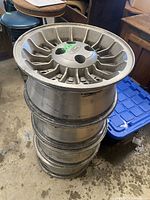 Photo showing four stacked aluminum Ford rims with visible wear and dirt, highlighting overall used condition and size.
