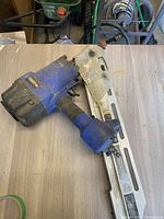 Photo of the full framing nailer on a wooden surface showing the blue and black body, the nail magazine rail and air hose connection.