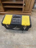 Closed black and yellow plastic toolbox with two metal clasps, some wear and dirt visible