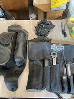 Overview of Harley-Davidson leather tool holder with tools, gloves, and satchel on table.