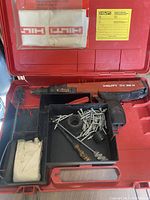 Open carrying case showing Hilti DX 36 M tool, fastening nails, cleaning brush, and accessory parts
