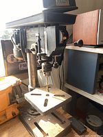 Full view of Jobmate corded drill press showing the drill bit in the chuck, the adjustable worktable and vertical column.