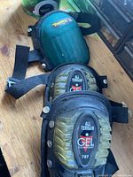 Two sets of knee pads on a wooden surface, one with gel cushioning labeled All Terrain Gel Comfort 707, the other green Tommyee with hard shell.