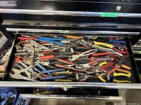 Drawer filled with assorted locking pliers, wrenches, and pliers in various colors and sizes.
